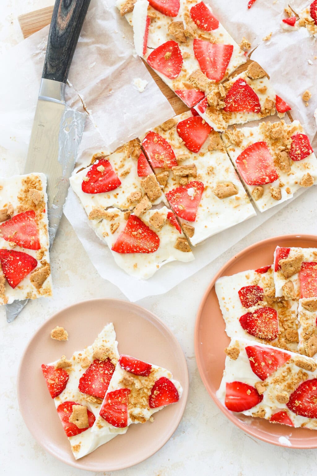 High Protein Frozen Greek Yogurt Cheesecake Bark with Strawberries on a pink plate with a knife and more cut pieces on the side