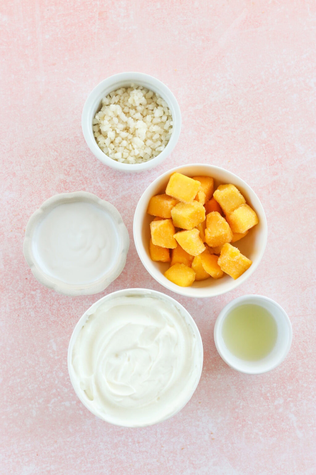 Ingredients for high protein tropical smoothie bowl with Greek yogurt in small white bowls, including Greek yogurt, mango, riced cauliflower, lime juice, milk of choice