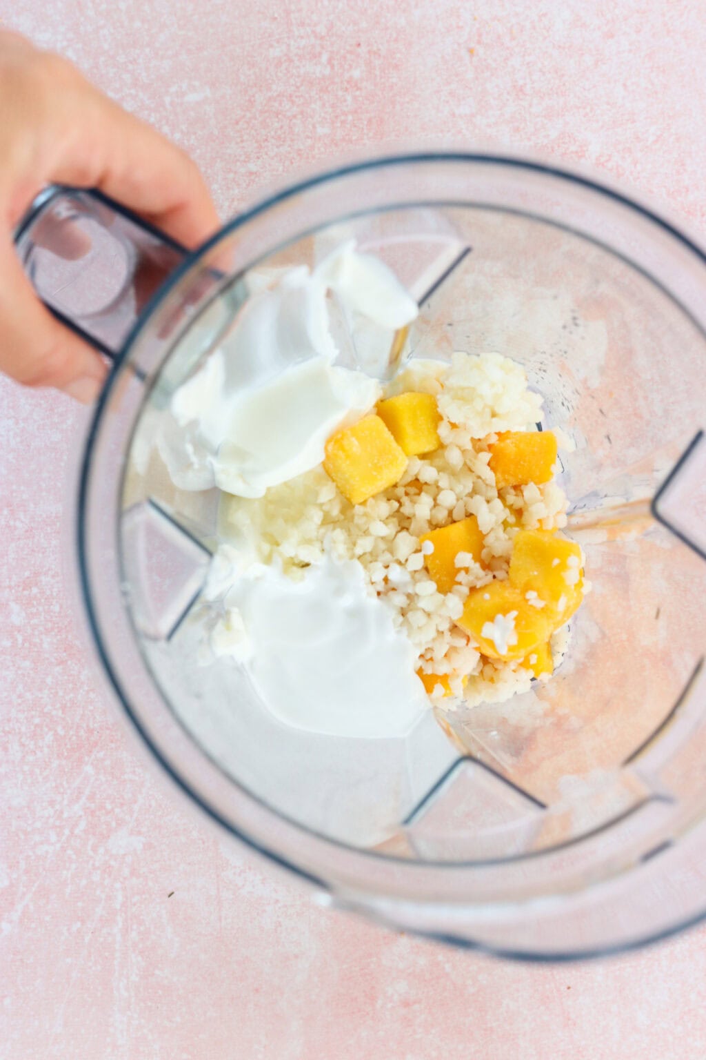 Ingredients for high protein tropical smoothie bowl with Greek yogurt unblended in a blender, including Greek yogurt, mango, riced cauliflower, lime juice, milk of choice