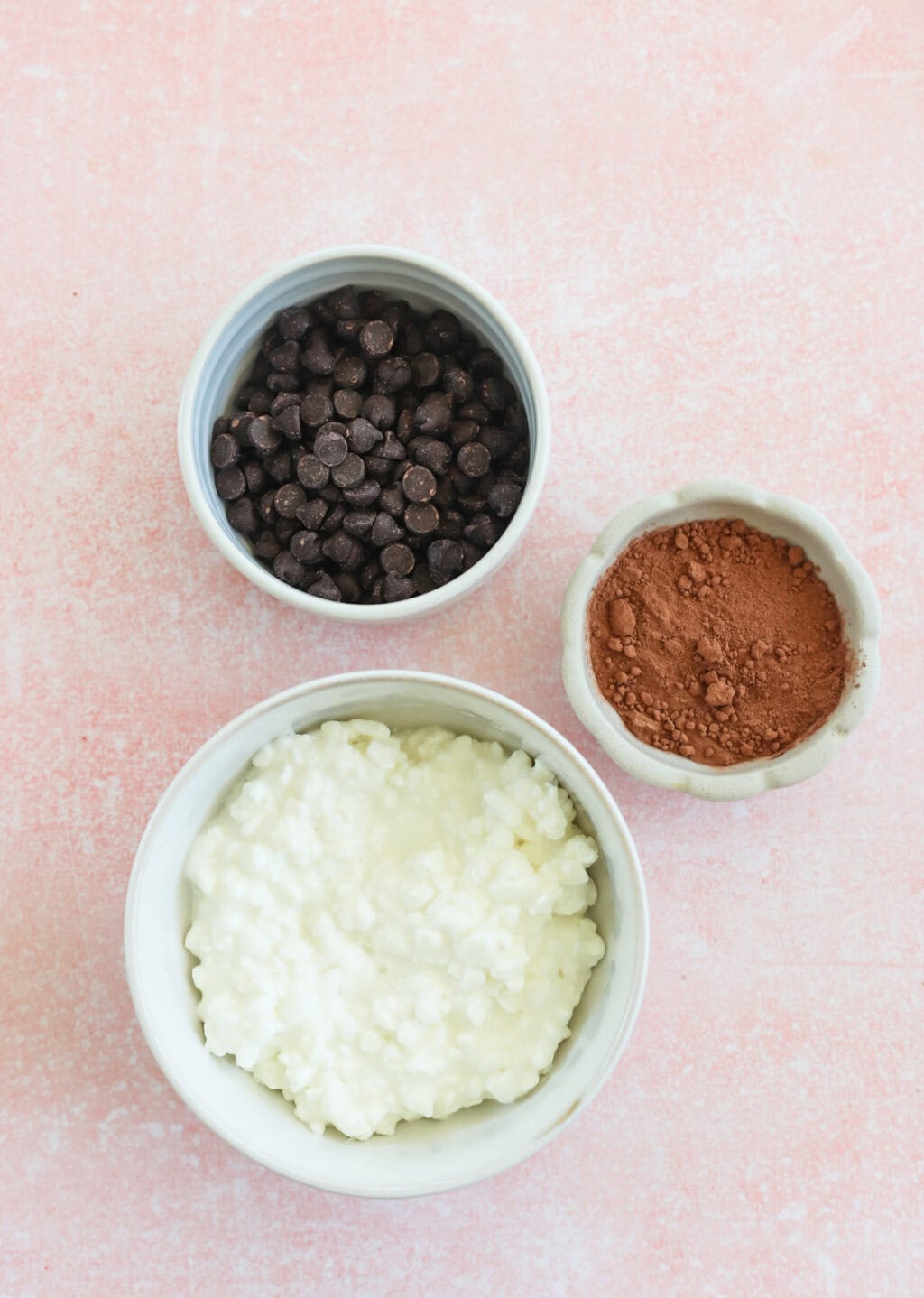Ingredients for 5-Minute Cottage Cheese Chocolate Mousse in small white bowls, including cottage cheese, chocolate chips, and cacao