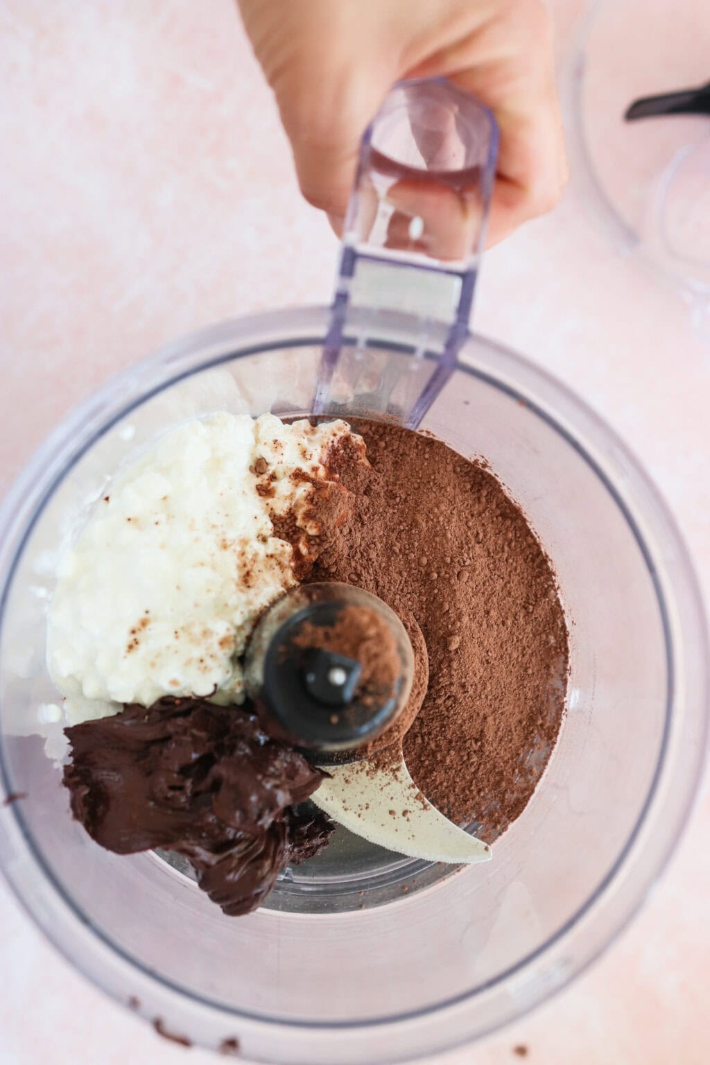 Ingredients for 5-Minute Cottage Cheese Chocolate Mousse unmixed in a food processor, including cottage cheese, chocolate chips, and cacao
