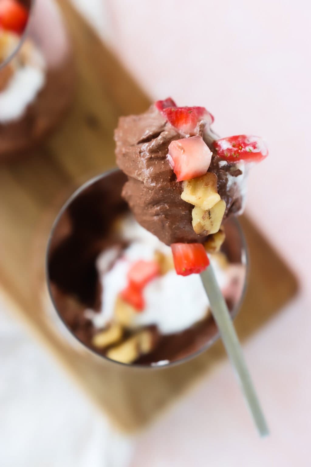 A spoonful of 5-Minute Cottage Cheese Chocolate Mousse with strawberries and walnuts with a glass cup in the background